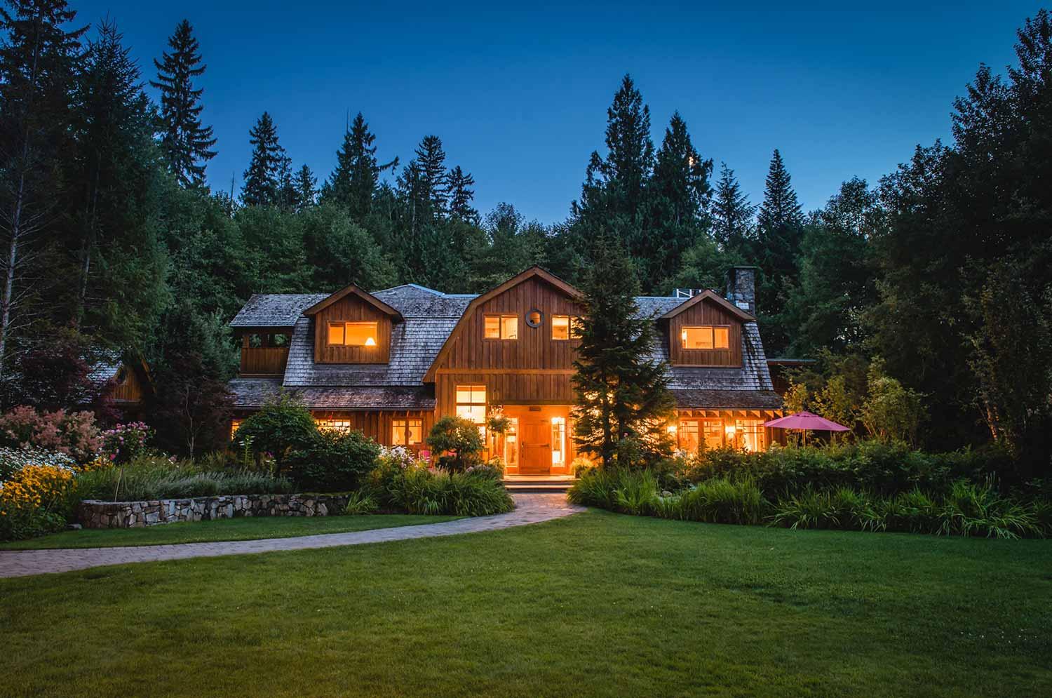 Wooden chalet lit up at dusk, surrounded by mountain forest