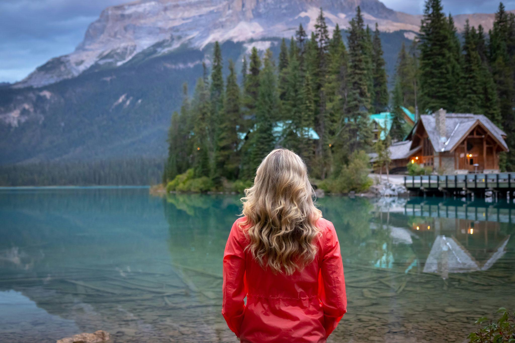 Woman looking out at a mountain lake toward a warmly lit chalet