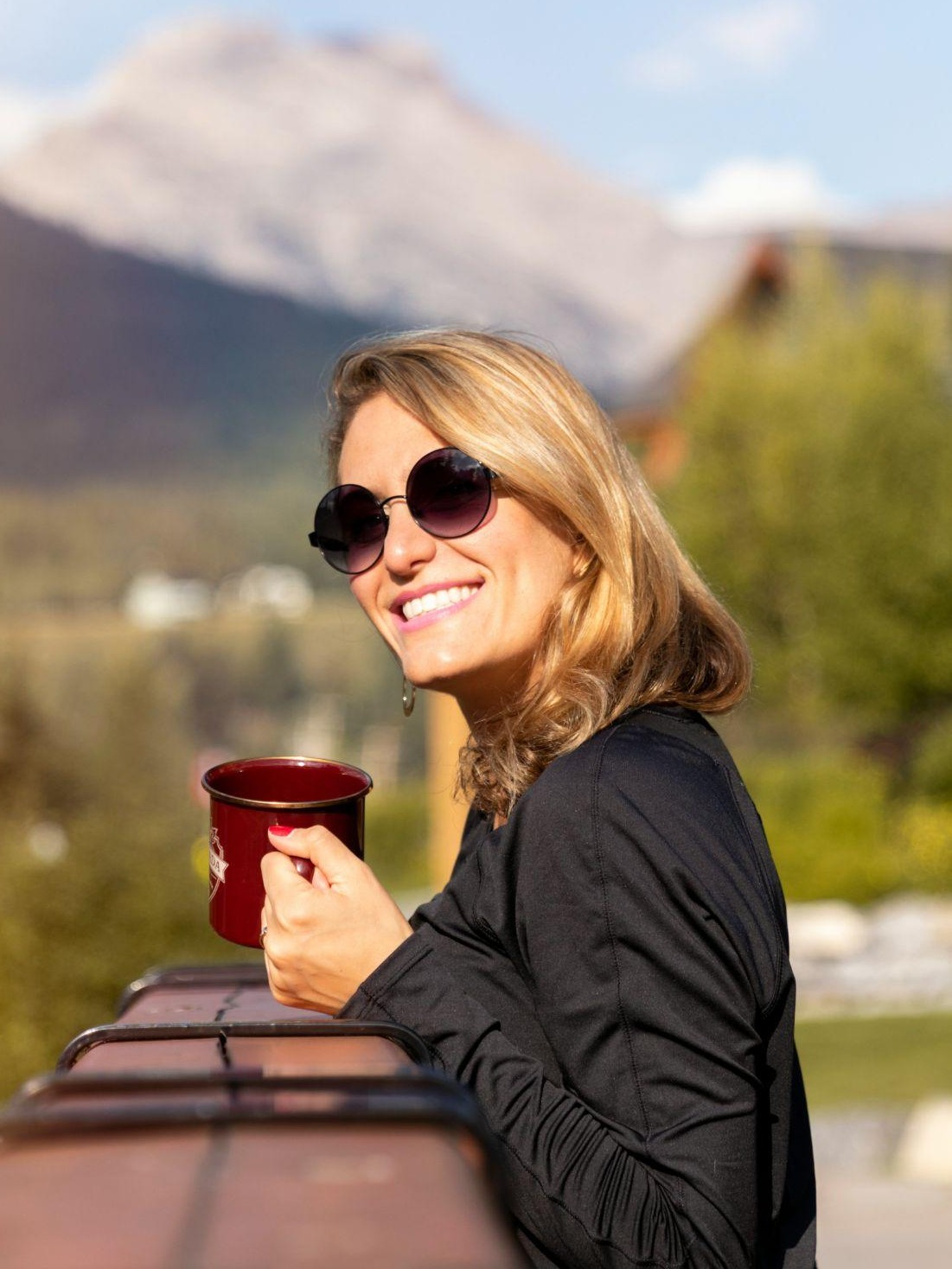 Woman holding a mug, smiling, mountains behind her